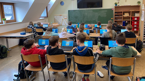 Foto einer Schulklasse in Rückenansicht, die eine Saferinternet.at-Schnitzejagd auf ihren Laptops lösen