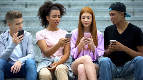 4 Jugendliche (2 Burschen und 2 Mädchen) sitzen auf einer Stiege und schauen irritiert auf ihre Smartphone. 