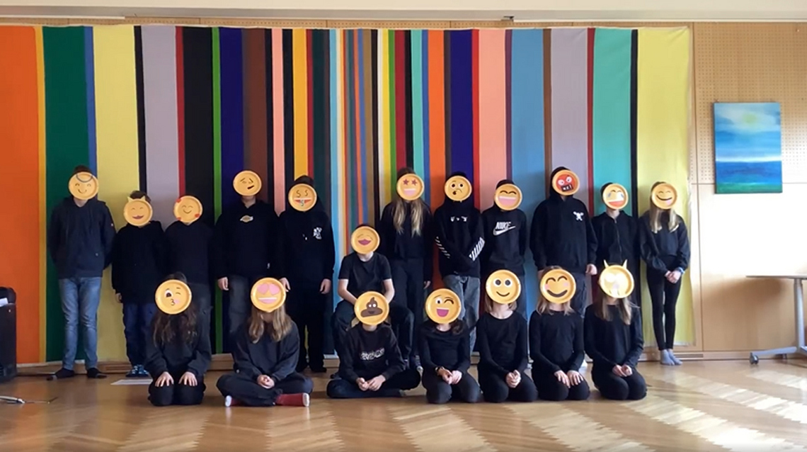 Gruppenfoto einer Klasse: Die Schüler:innen sind schwarz gekleidet und halten Emoji-Masken vor ihre Gesichter