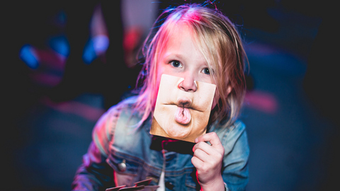 Bild von einem Kind, das vor ihrem Gesicht ein Foto von anderen Lippen hält. 