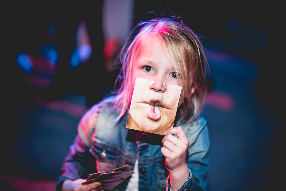 Bild von einem Kind, das vor ihrem Gesicht ein Foto von anderen Lippen hält. 